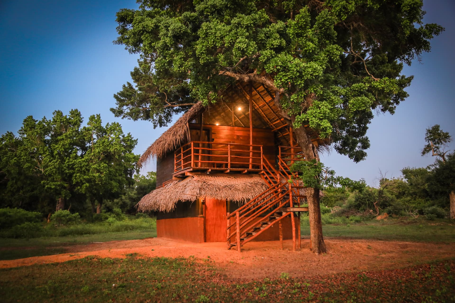 A serene bedroom with a double bed, soft mosquito net, and a view onto the wooden balcony overlooking the garden.